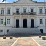 Edifício governamental em Natal, RN, com bandeiras do Brasil e do estado, representando eleições e apoio político.