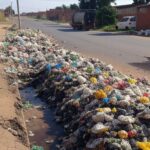 Rua em Ceilândia com lixo sendo removido por caminhões, destacando falhas na infraestrutura do DF.