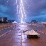 Raio atingindo evento em Brasília durante tempestade, expondo falhas em protocolos de segurança, com estruturas modernas ao fundo.