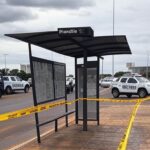 Parada de ônibus isolada com fita policial no DF, cena de investigação de morte, sem pessoas.