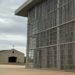 Fachada de prisão federal no Brasil com elementos religiosos ao fundo, representando solicitação de assistência espiritual.