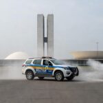 Cena de confronto com viaturas da PM no DF, nuvens de spray de pimenta no ar em rua de Brasília.
