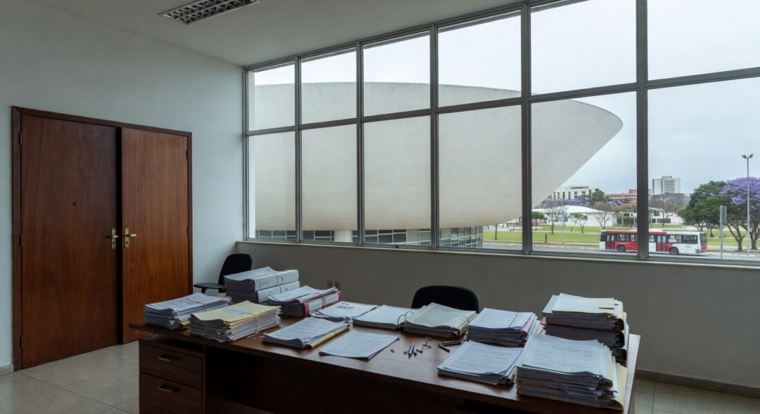 Edifício moderno em Brasília com pilhas de documentos burocráticos, ilustrando exclusão de associações de consumidores pela Caesb e Adasa.