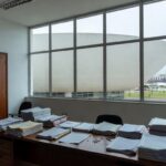 Edifício moderno em Brasília com pilhas de documentos burocráticos, ilustrando exclusão de associações de consumidores pela Caesb e Adasa.