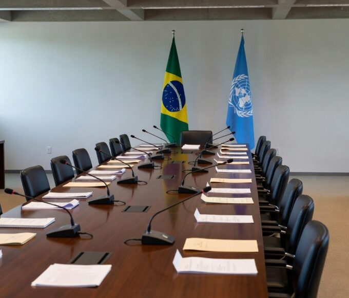 Sala de conferência em Brasília com bandeiras do Brasil e ONU, representando críticas a guerras, fome e descrédito da ONU.