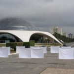 Fachada da Câmara Legislativa do DF com bandeiras roxas, expondo persistência da violência contra mulheres em evento.