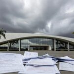 Edifício da CLDF em Brasília com documentos de seguros, simbolizando homenagem e críticas por distrações legislativas.
