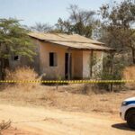 Cena de crime em casa residencial em Águas Lindas, Goiás, com viaturas policiais e fita de isolamento, sem pessoas.