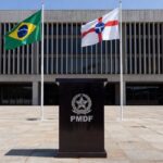 Salão cerimonial no Palácio do Buriti com bandeiras do Brasil e DF, pódio e símbolos de justiça e PMDF em Brasília.